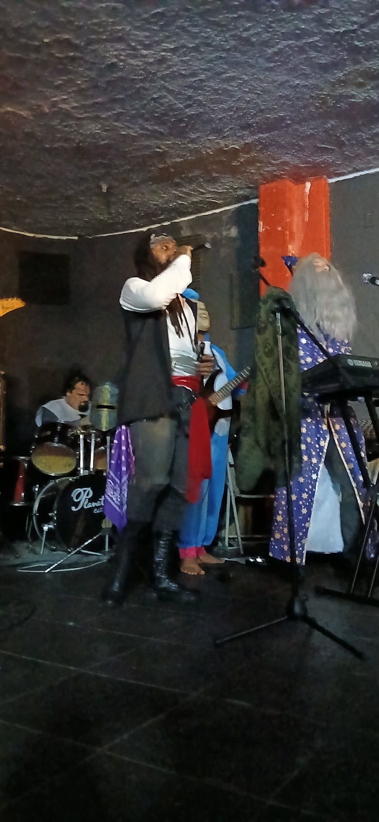 Arthas Gaius, capitão pirata e vocalista, no palco com microfone e faixa vermelha.